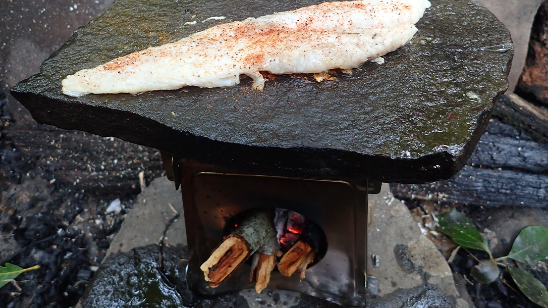 Use a raised rock over a small twig stove to maximize cooking surface and allow larger fuel while masking smoke.