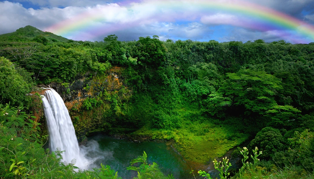Sunlight streams through emerald cliffs as waterfalls plunge into the lush valleys of Kauai’s Na Pali Coast.