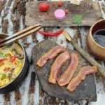 Bacon sizzling on a heated rock over a glowing campfire—nature’s skillet at work.